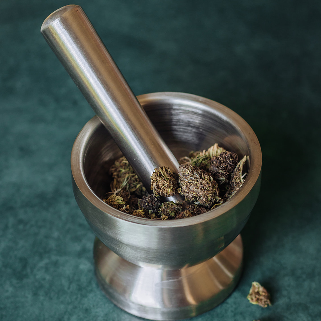 a mortar and pestle made of stainless steel holds dried hemp flower buds