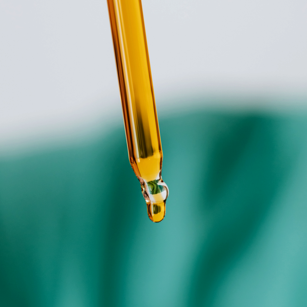 Hemp essential oil dripping out of a pipette against a white and green blurred background.