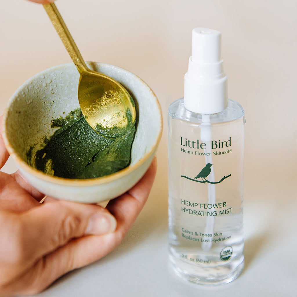 Hemp Flower Hydrating Mist clear bottle with spoon and bowl containing green hemp flower paste